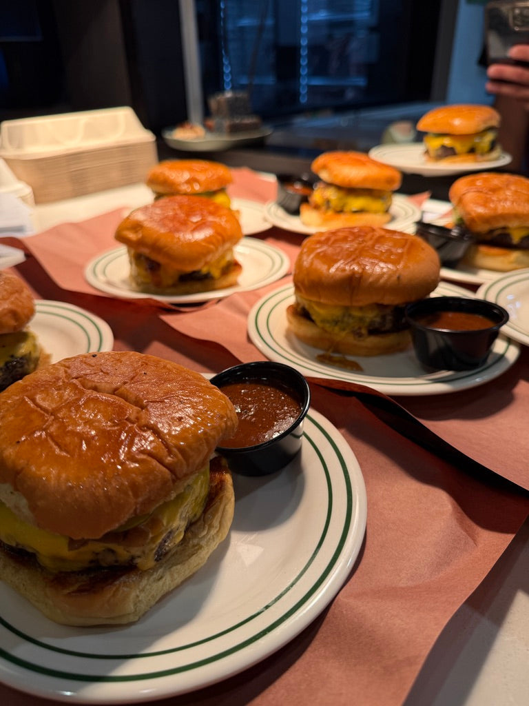 Multiple burgers on plates with side dishes on a table.